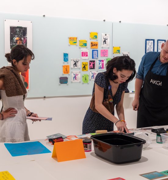 A man wearing an apron helping two women with an art project