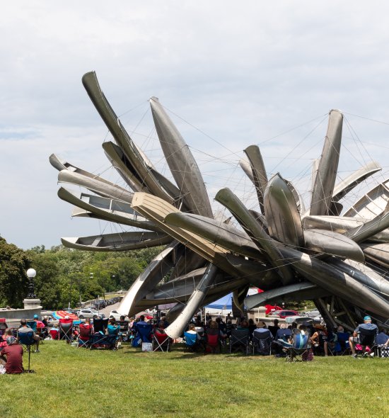 People in lawn chairs sitting around a large outdoor sculpture
