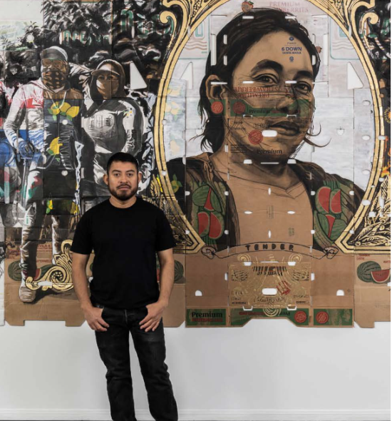 A person all black stands in front of an artwork of figures rendered on cardboard boxes