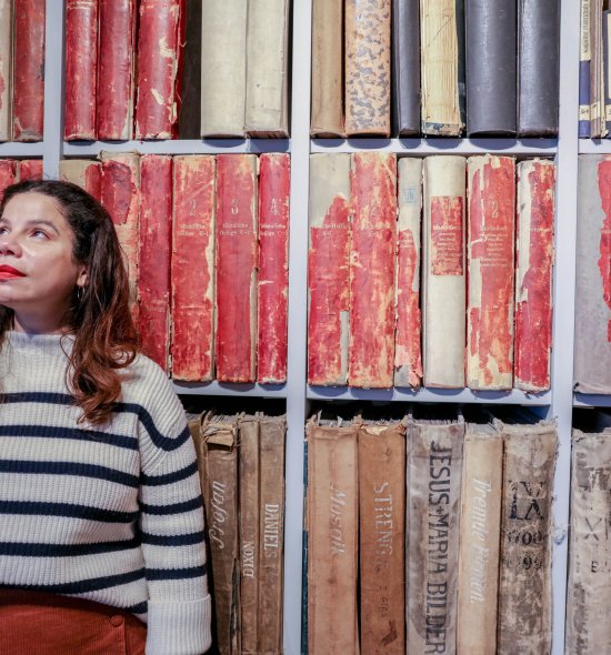 A person in a striped shirt looking to the left while standing in front of a mosaic background
