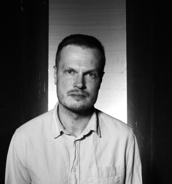 Black and white photo of a man with dark hair, light eyes, a mustache, and fair skin wearing a white button down shirt 