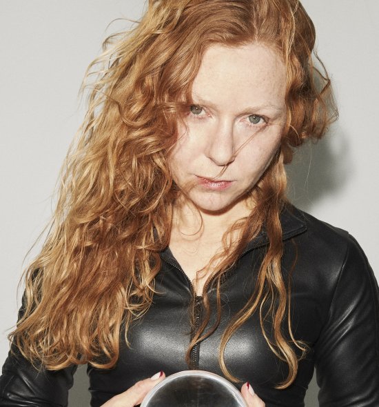 Photo of a woman with long wavy red hair, fair skin and green eyes wearing a black zip up