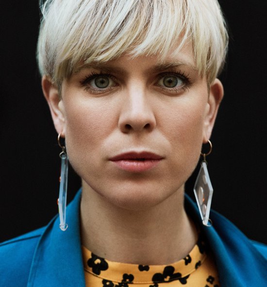 Headshot of a woman with short bleach blonde hair and fair skin in a yellow and blue shirt 