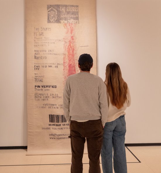 Two people standing in front of a large artwork resembling a receipt 