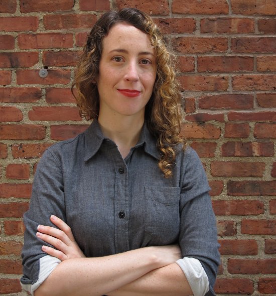 A person with their arms folded, standing in front of a brick wall