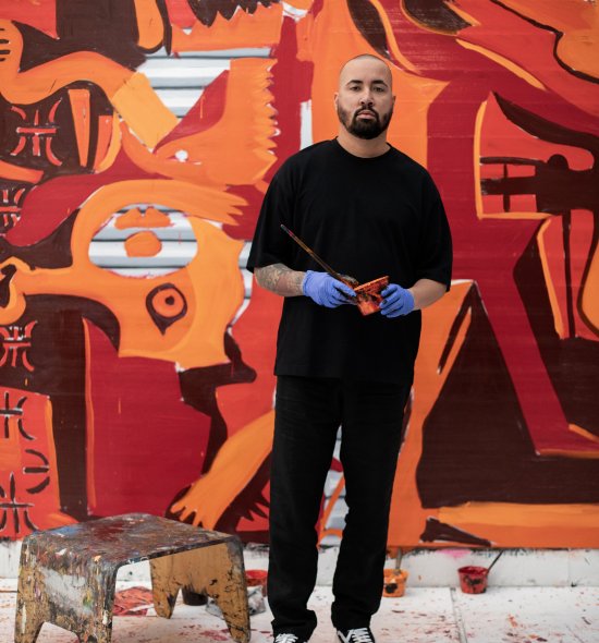 A person in all black and standing in front of a vibrant orange and red mural