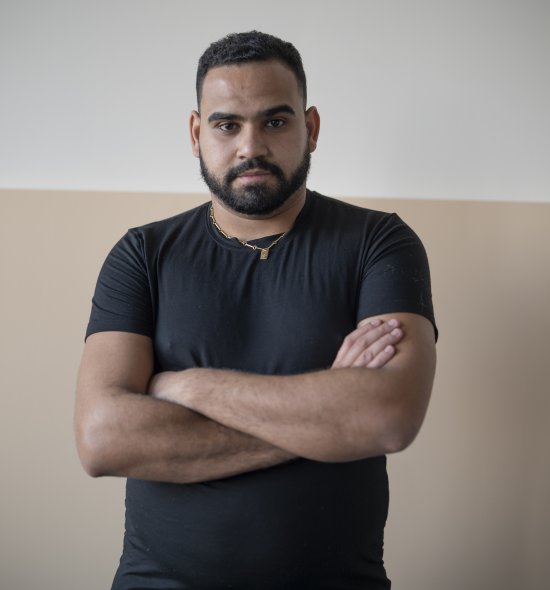 A person with their arms crossed standing in front of a blank wall with a blank canvas leaning on it