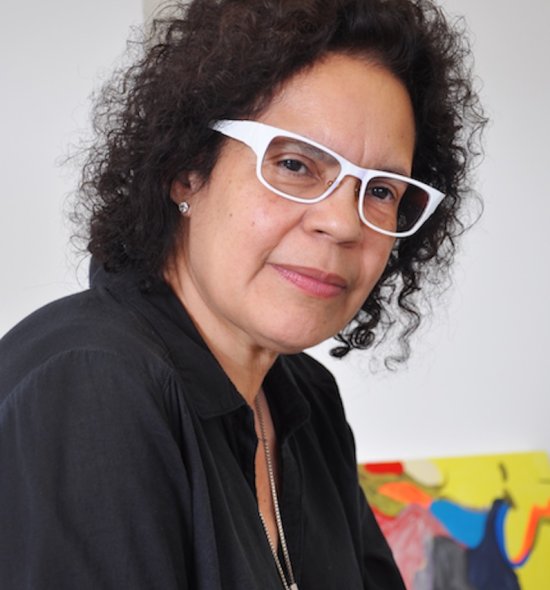 A person with dark shoulder length curly hair wearing a black shirt and white framed glasses