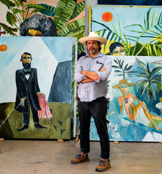 A person wearing a large white hat, standing in a room filled with large vibrant paintings