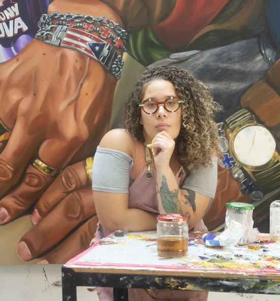 A person leaning on an artist table with their head resting in their hand and a large painting behind them