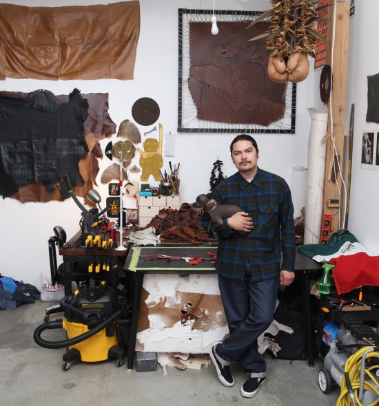 A person holding a small dog in the middle of an art studio with various leather works
