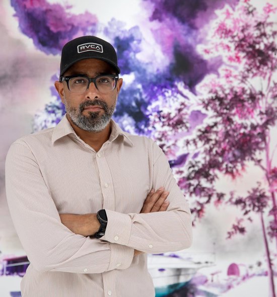 A person wearing a black hat and glasses standing in front of a bright, purple, painting