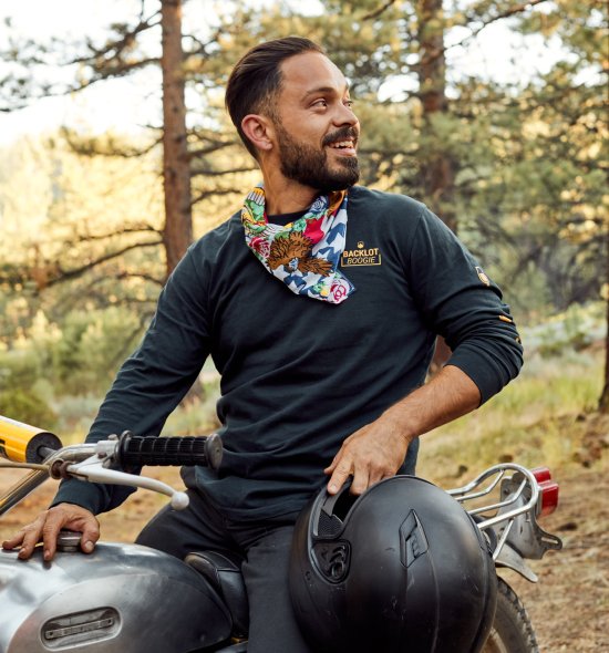 A person sitting on a dirt bike with a helmet in their hand, looking off to the right smiling