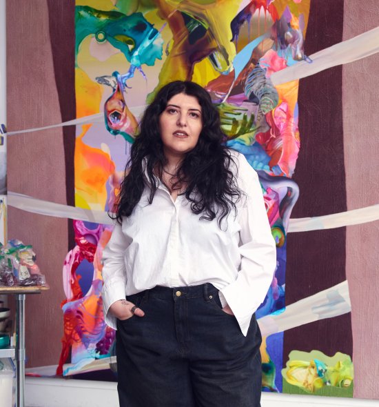 A person wearing a white shirt and black pants standing in front of a vibrant artwork