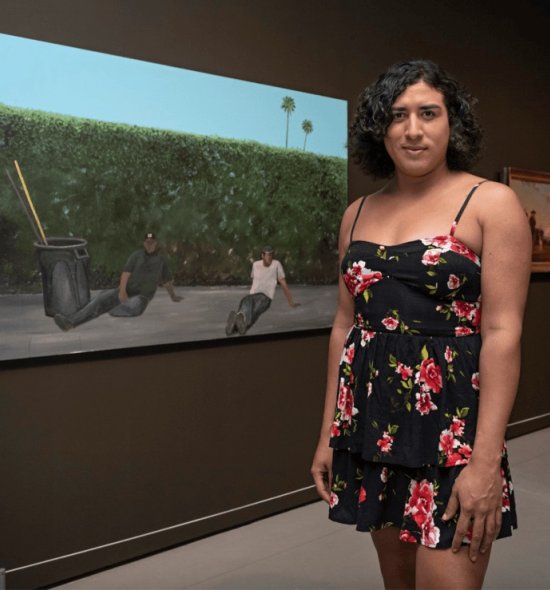 A person in a floral dress standing in front of a painting of two people sitting on the ground next to maintenance supplies in front of greenery
