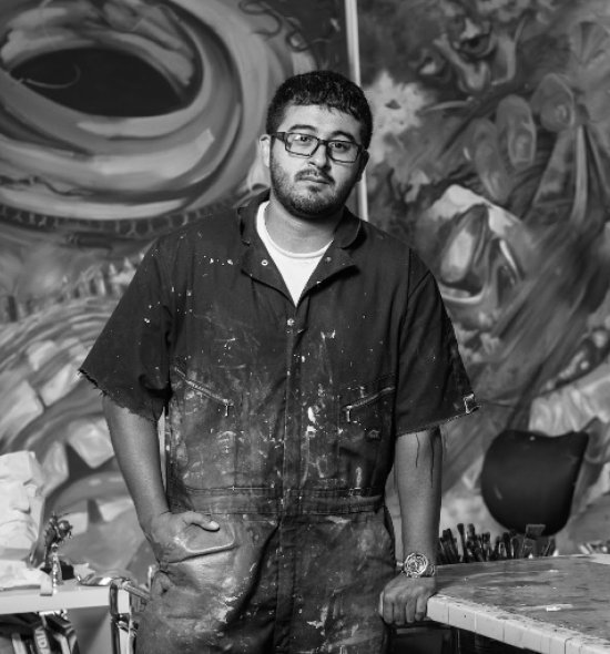 Black and white image of an artist with paint covered overalls in a studio