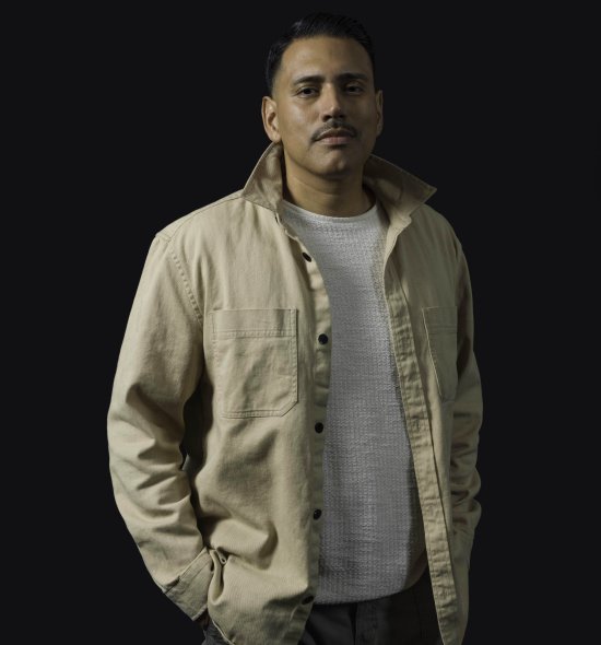 A person with a button down shirt and popped collar in front of a dark backdrop with dark lighting