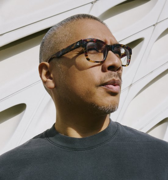 A closeup of a person in direct sunlight looking to the side, wearing tortoise shell glasses