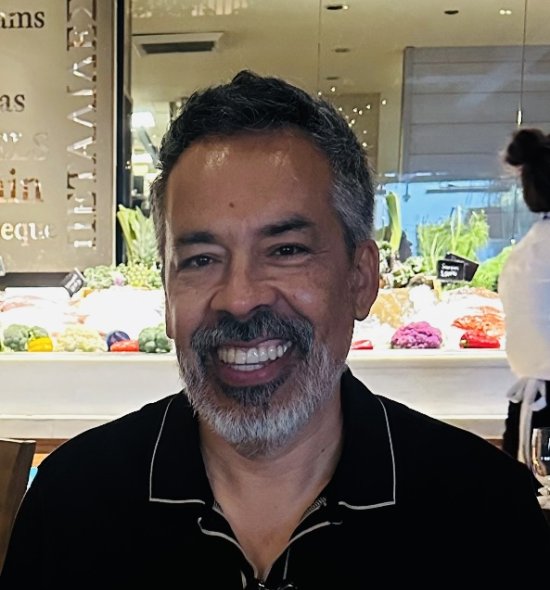 A person with salt and pepper short hair and facial hair, smiling at the camera