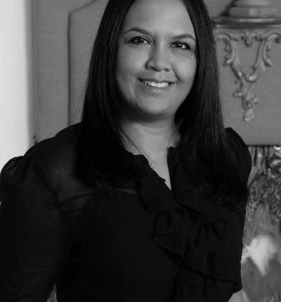 A black and white headshot of a person in all black smiling with medium length dark hair