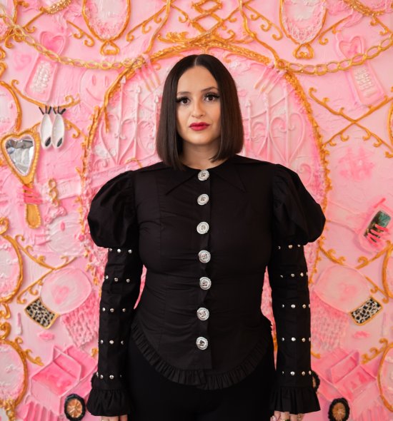 A person in a black button blouse with dramatic sleeves standing in front of a pink painting 