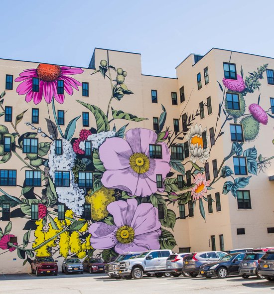 A large mural featuring pink, yellow, and white wildflowers on a large tan building