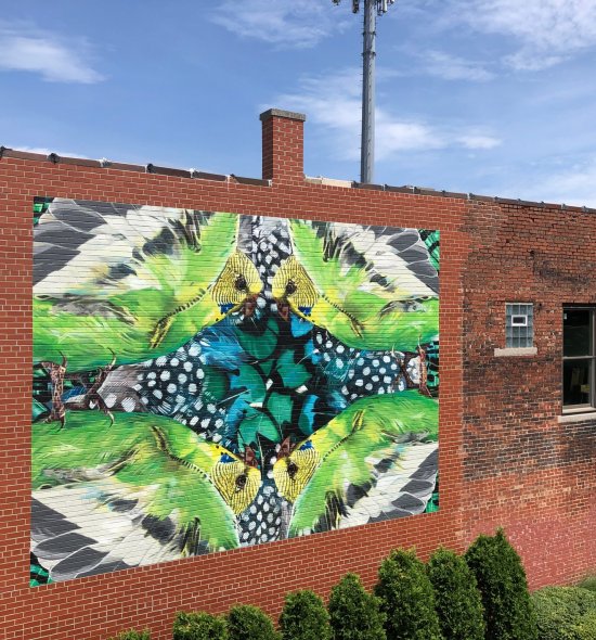 A red brick building with a mural on the side that looks like a kaleidoscope of bird feathers and butterfly wings