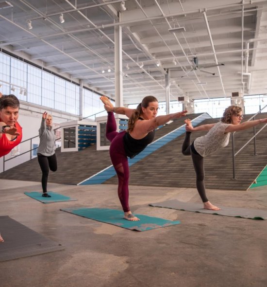 Four women doing yoga poses in front of a rooftop built inside a large industrial building