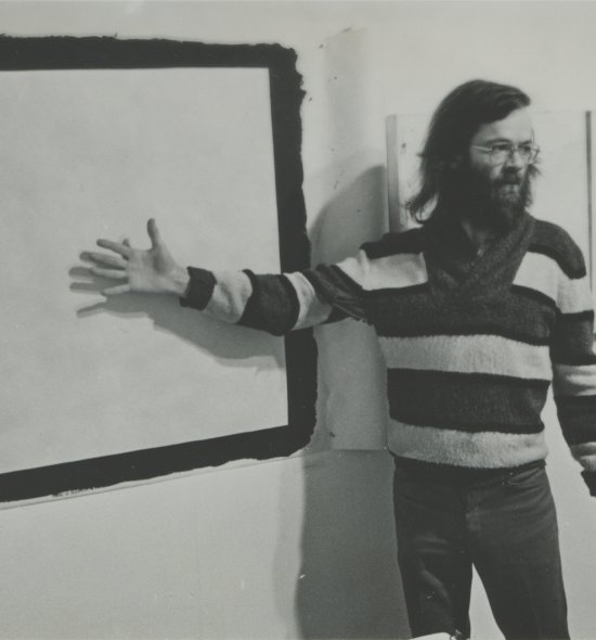 Film photo of a man in a striped sweater pointing at a board